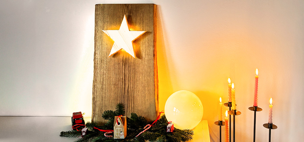 Ein beleuchteter Holzstern ist in eine große Holzplatte eingelassen, dekoriert mit Tannenzweigen und Kerzen.