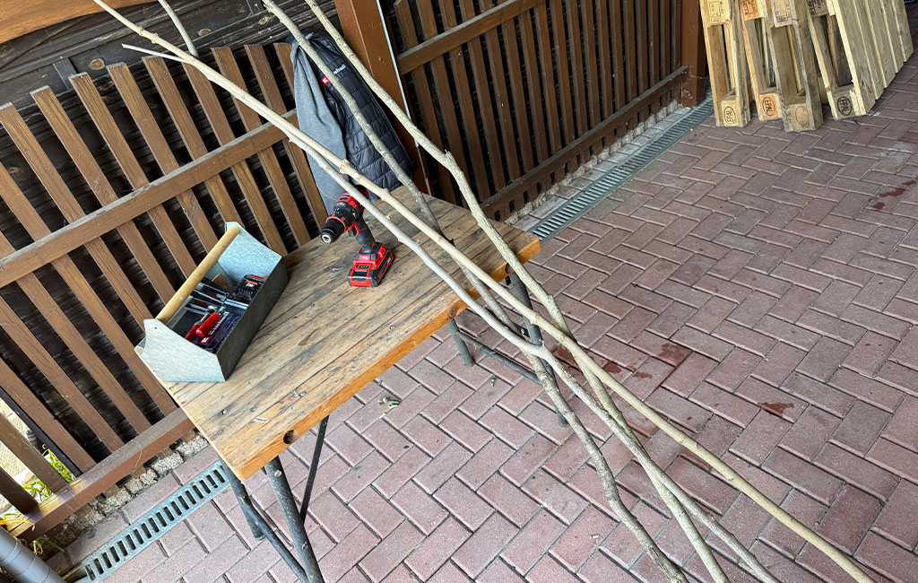 Several long branches, a toolbox, and a cordless drill lie on a workbench.