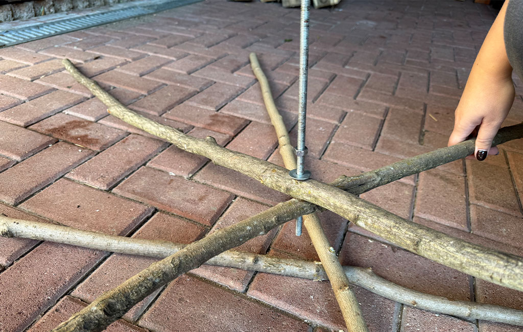 Several branches are connected in a star shape with a long threaded rod; one hand holds a branch.