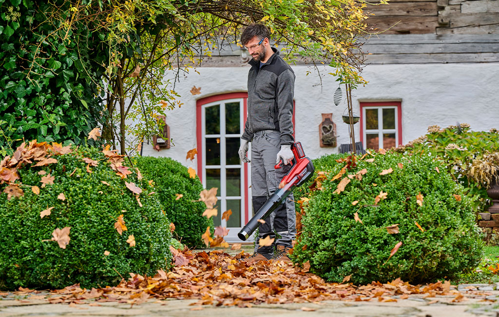A man clears autumn leaves with a Einhell cordless leaf blower in front of a house.