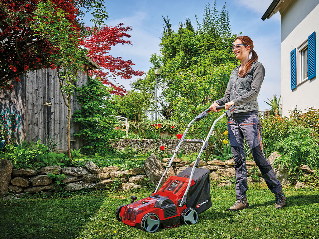 A woman doing lawn care with her Einhell cordless scarifier aerator.
