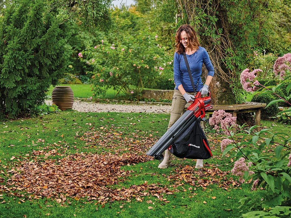 Eine Frau im Garten beim Aufsaugen von Herbstlaub mit einem Einhell Akku-Laubsauger.