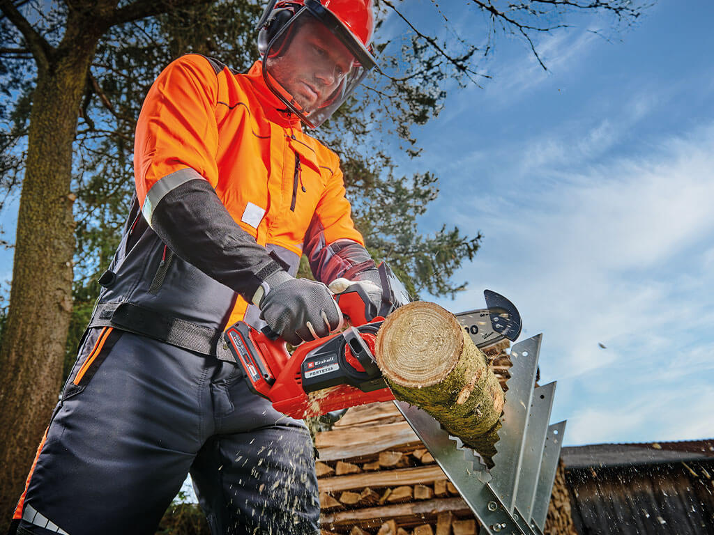 A man sawing through a tree trunk with a top-handled cordless chainsaw from Einhell.