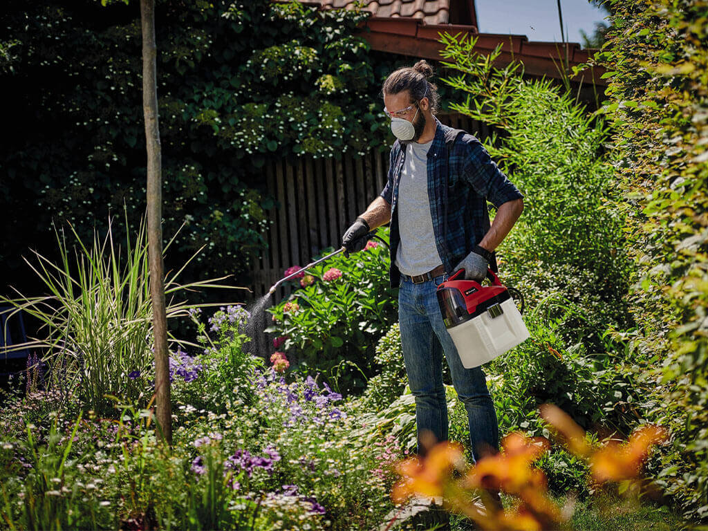A man waters his plants with the help of a cordless pressure sprayer from Einhell.