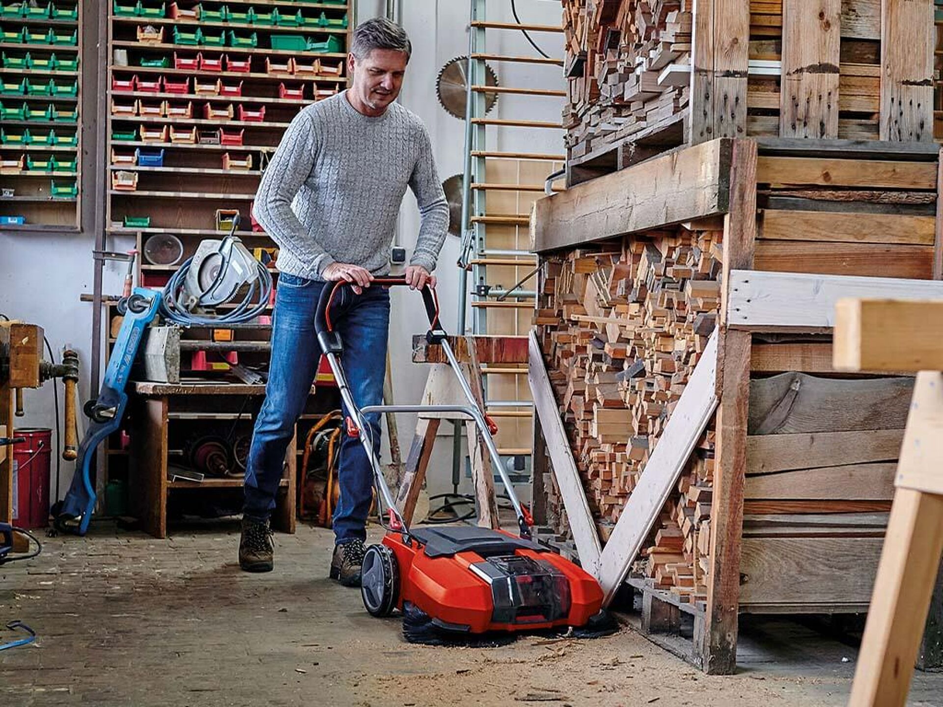 Ein Mann fegt seine Werkstatt mit einer Einhell Kehrmaschine.