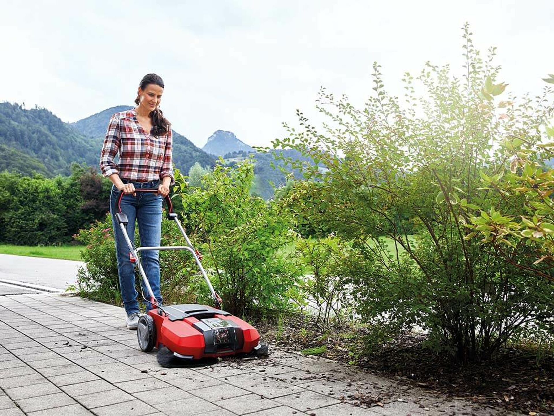 eine Frau kehrt ihre Hofeinfahrt mit einer Kehrmaschine