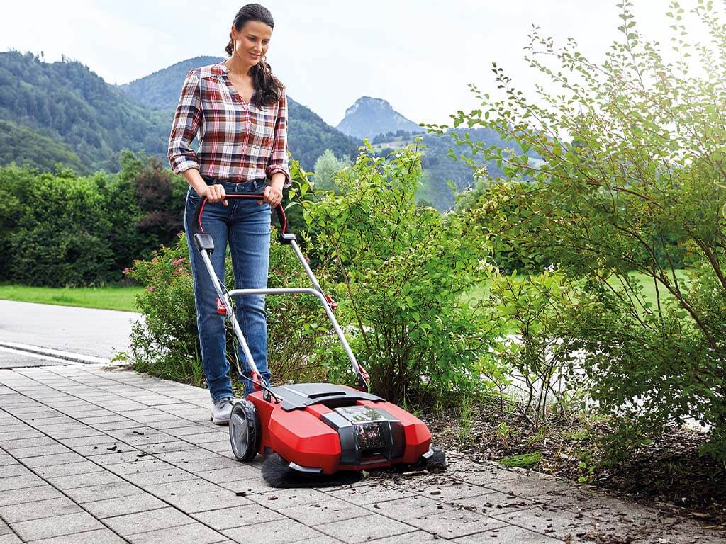 A woman sweeps a driveway with the Einhell sweeper