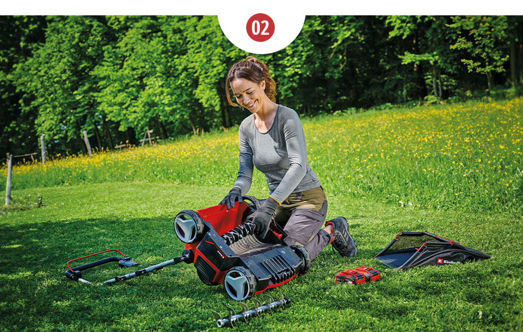 A woman kneels in front of a scarifier and replaces a blade roller with an aerator roller.