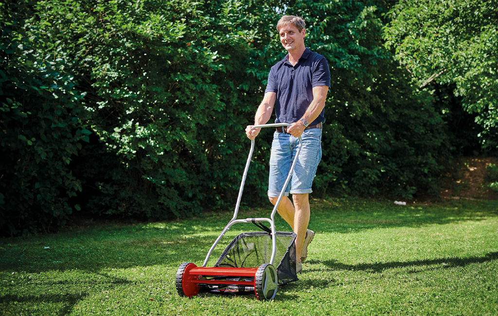 A man mows the lawn in a garden with an Einhell hand lawn mower.