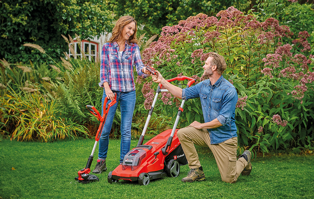A man kneels next to a woman in a garden and hands her a Power X-Change battery.