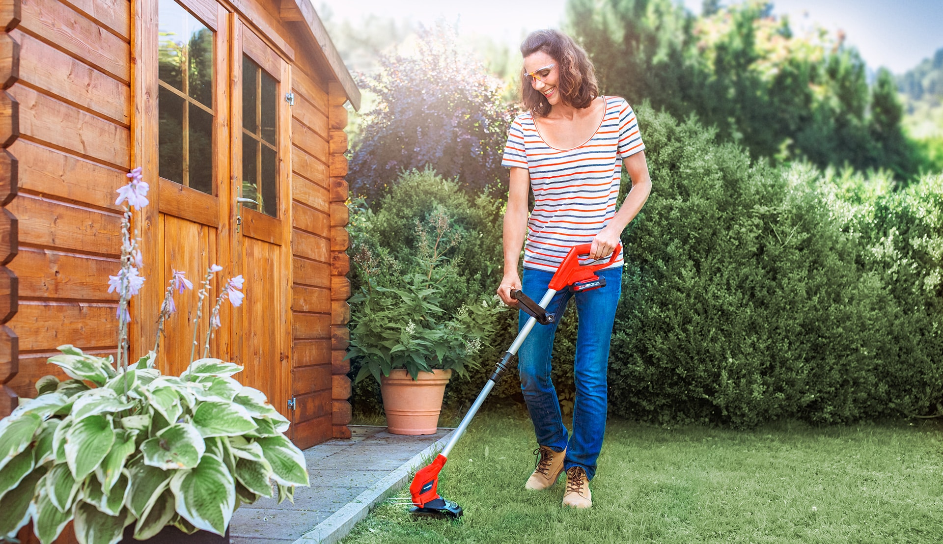 A woman trims the edge of the lawn in a garden with a cordless lawn trimmer from Einhell.
