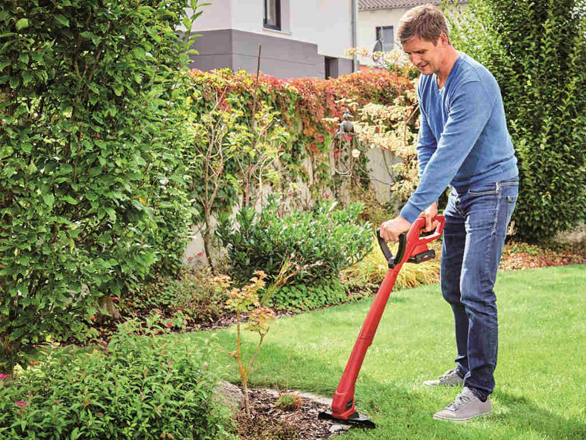 Ein Mann trimmt die Rasenränder in einem Garten mit einem Akku-Rasentrimmer von Einhell.