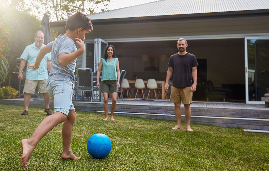 Drei Erwachsene und ein Kind spielen zusammen Fußball in einem Garten