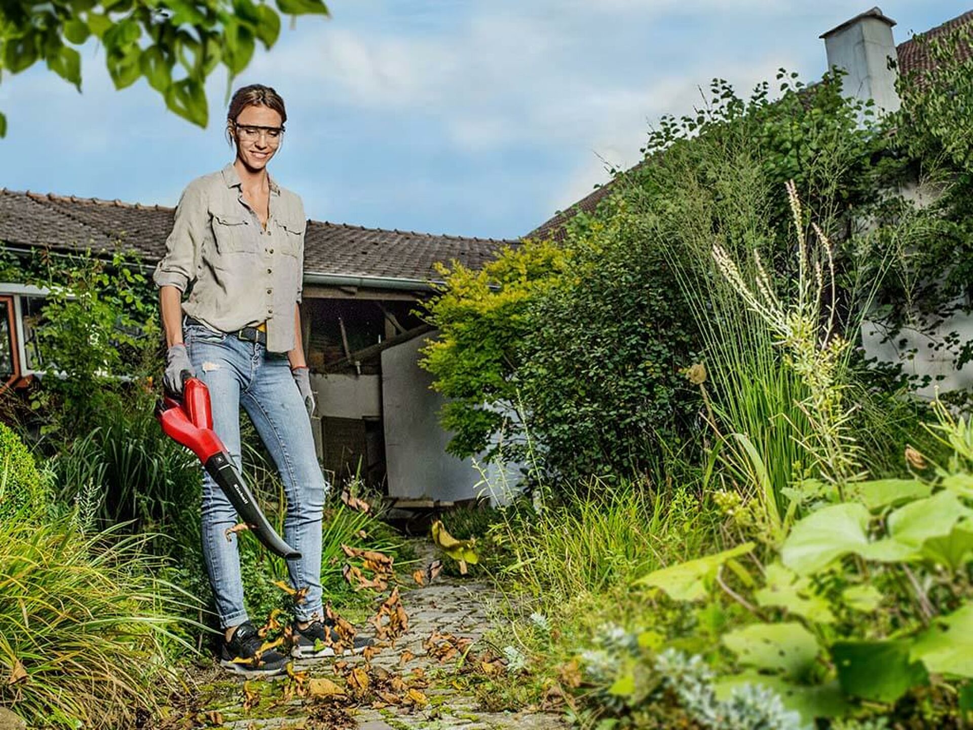 Eine Frau bläst das Laub auf einem Gehweg mit einem Einhell Akku-Laubbläser weg.