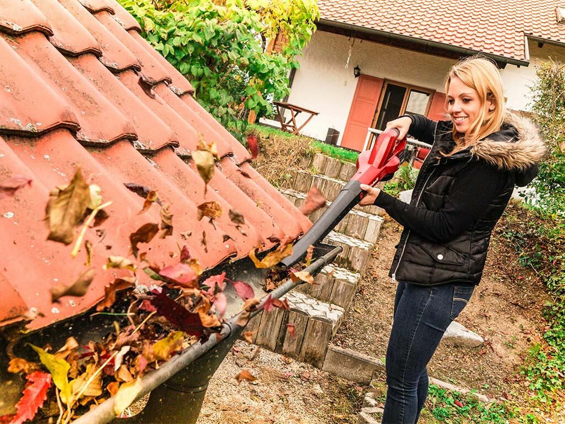 Eine Frau bläst mit einem Akku-Laubbläser von Einhell das Laub aus einer Dachrinne.