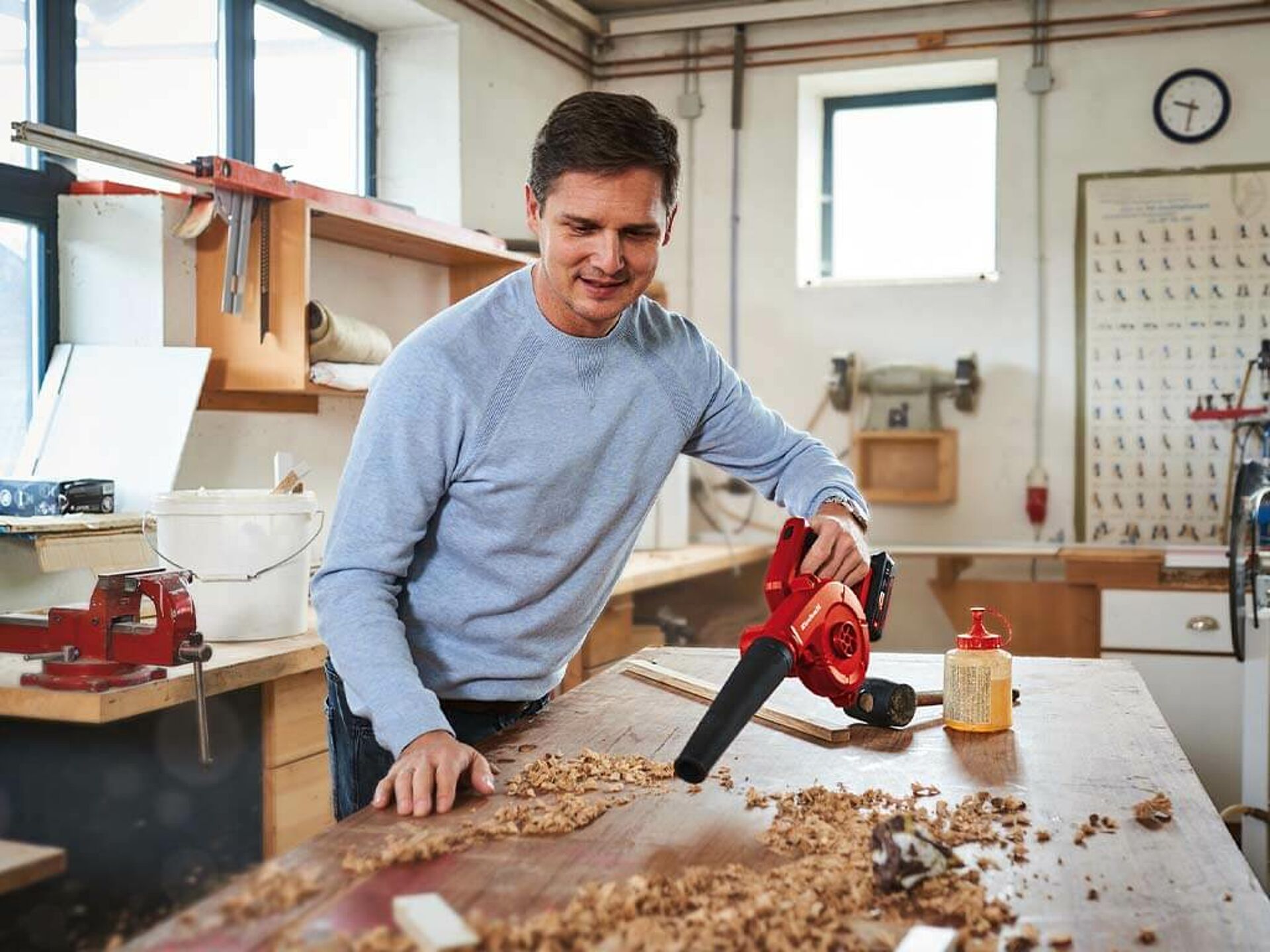 Ein Mann bläst Sägemehl von seiner Werkbank mit einem Einhell Akku-Laubbläser weg.