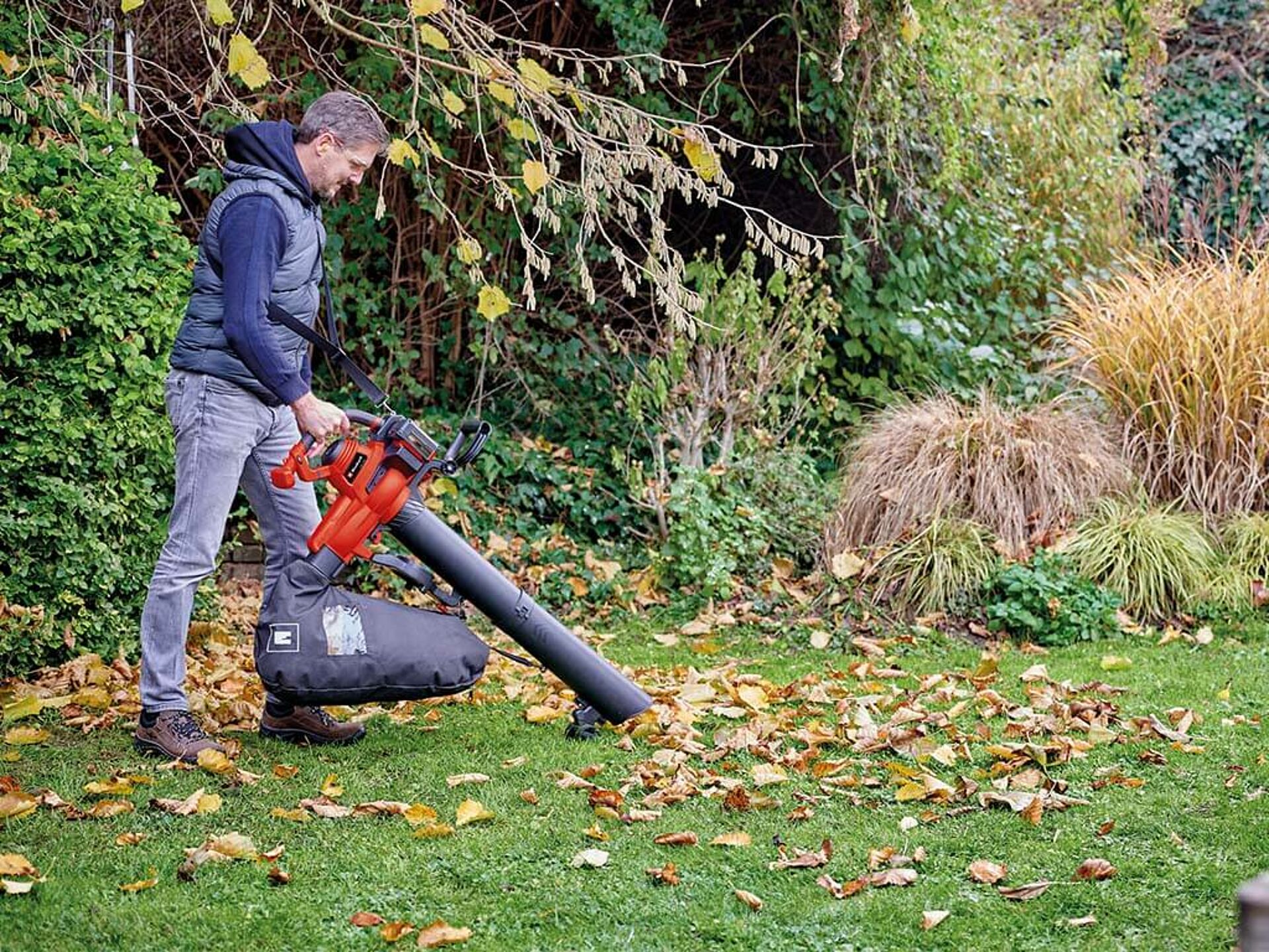 A man vacuums up leaves in a garden with an Einhell leaf vacuum.