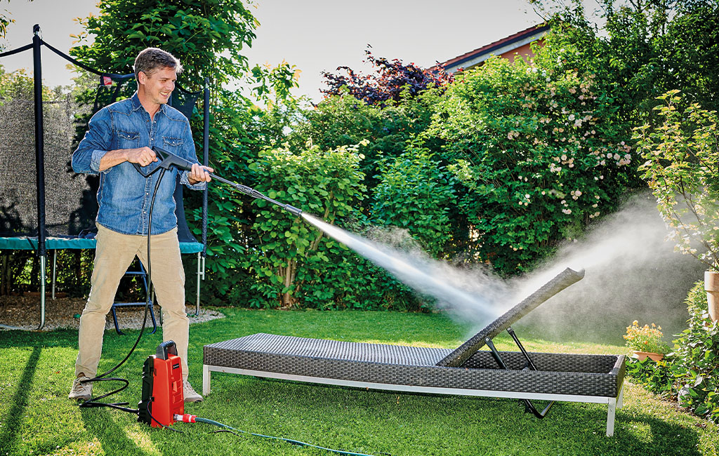 ein Mann reinigt eine Gartenliege mit dem Einhell Hochdruckreiniger