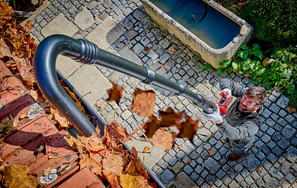 ein Mann reinigt eine Dachrinne mit dem Einhell Akku-Laubbläser