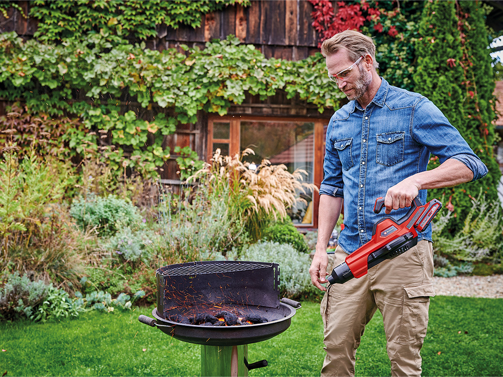 A man is using the einhell cordless blower to light the grill
