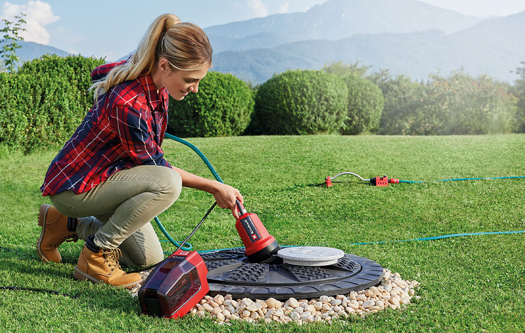 eine Frau pumpt Wasser aus einer Zisterne mit der Einhell Akku-Klarwasserpumpe