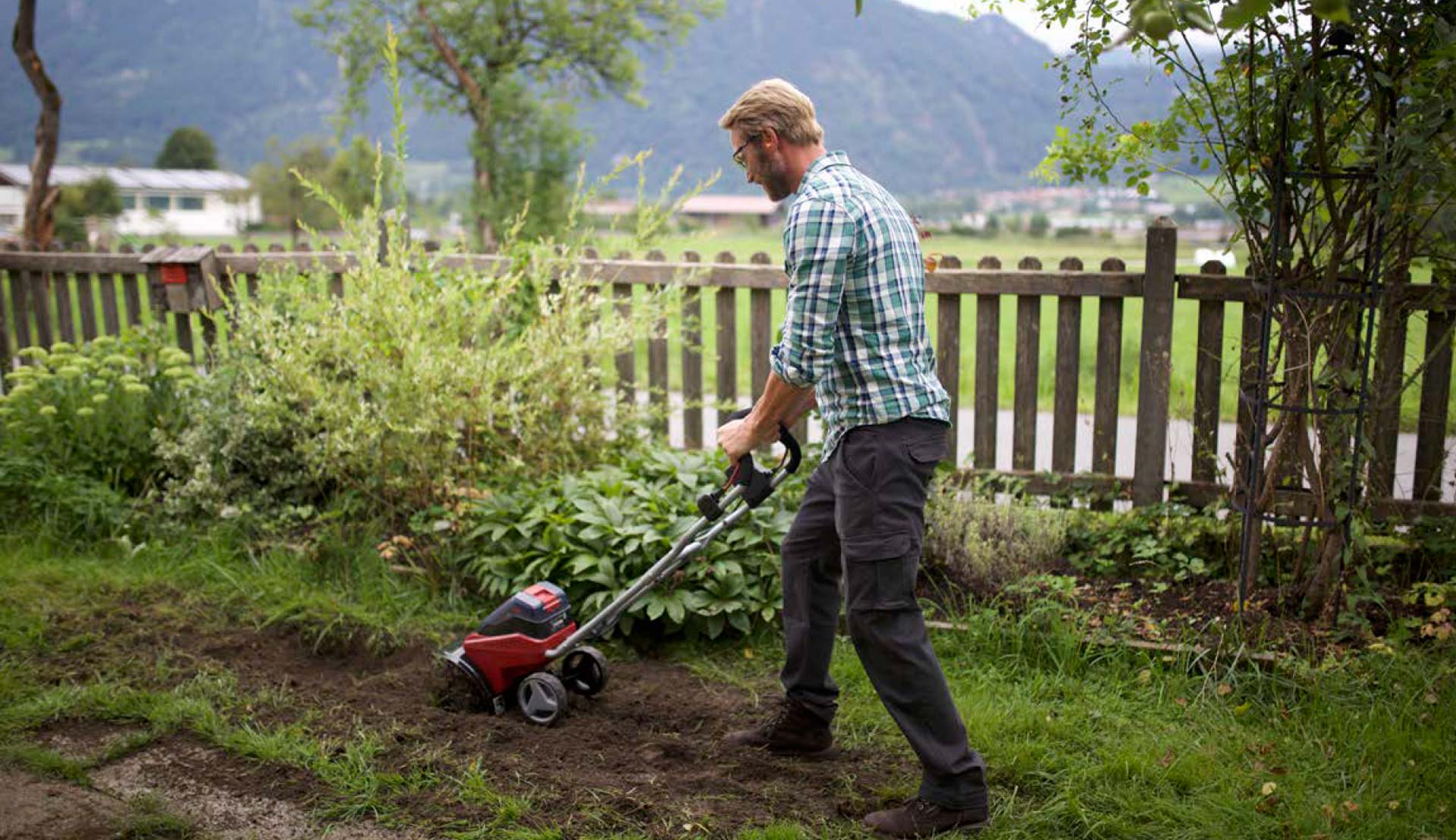 A man is using an Einhell cordless tiller in his garden to loosen up the soil