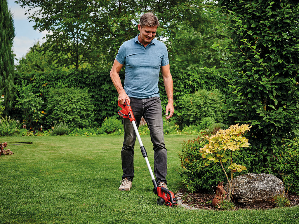 a man is trimming edges in his garden with a Einhell cordless grass- and bush shear