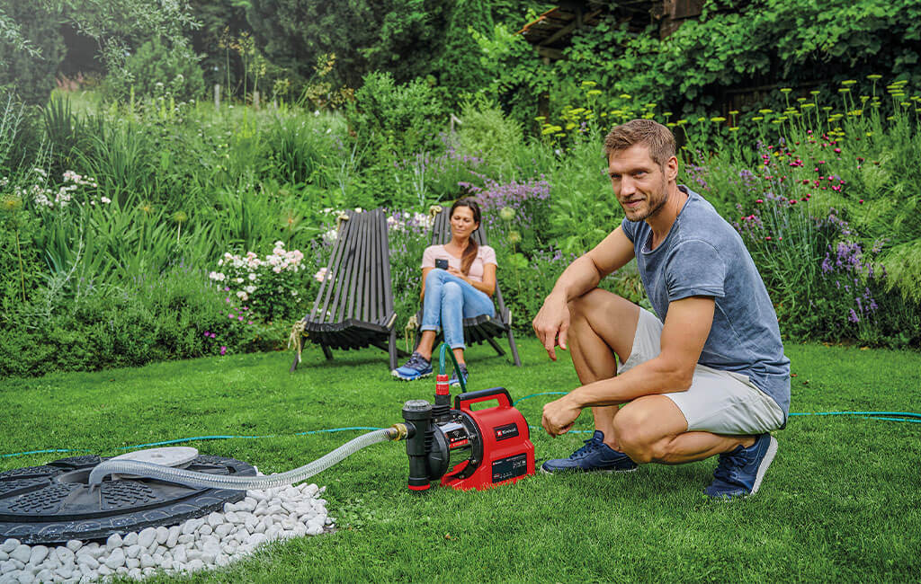 Ein Mann kniet und eine Frau sitzt neben einer smarten Gartenpumpe.