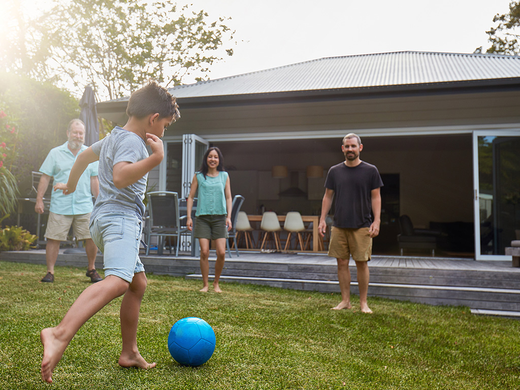 Child plays football with three adults on freshly mown lawn