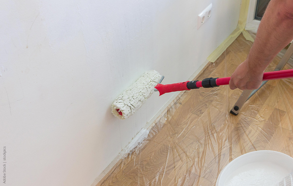 A white wall is painted with a paint roller, the floor is covered with foil