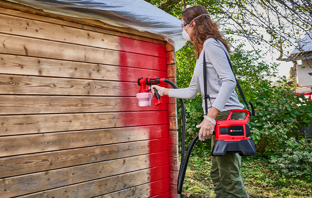 A man sprays a wall with yellow paint using a paint spray system.