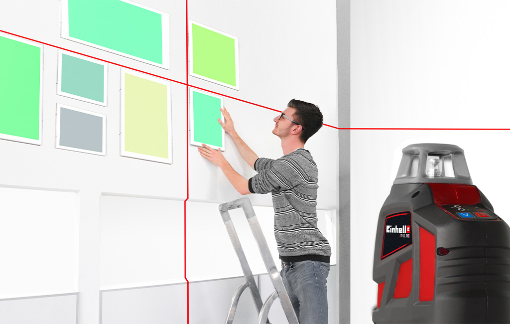 A man aligns pictures on a wall using a cross-line laser.