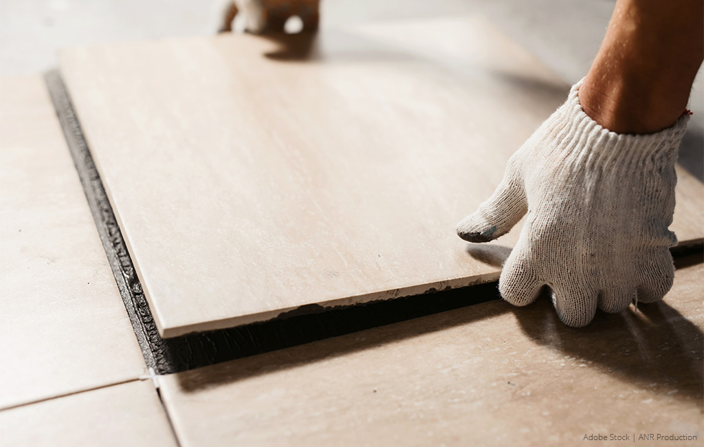 Ein Handwerker setzt eine neue Bodenfliese auf den vorbereiteten Kleber und richtet sie aus.