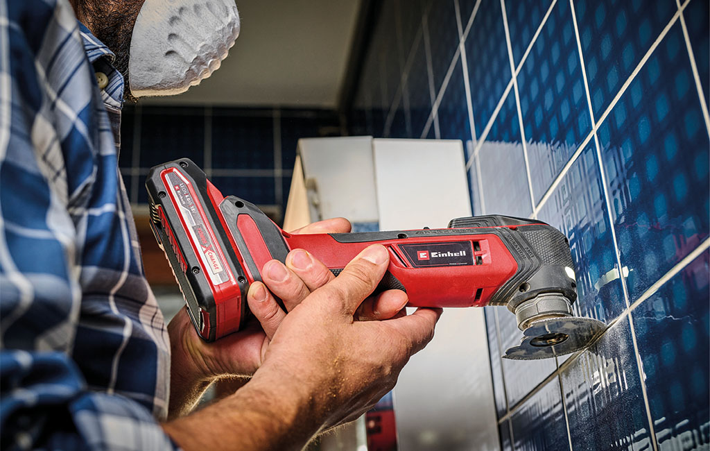 Ein Handwerker bearbeitet die Fugen dunkler Wandfliesen mit einem Einhell Akku-Multitool.