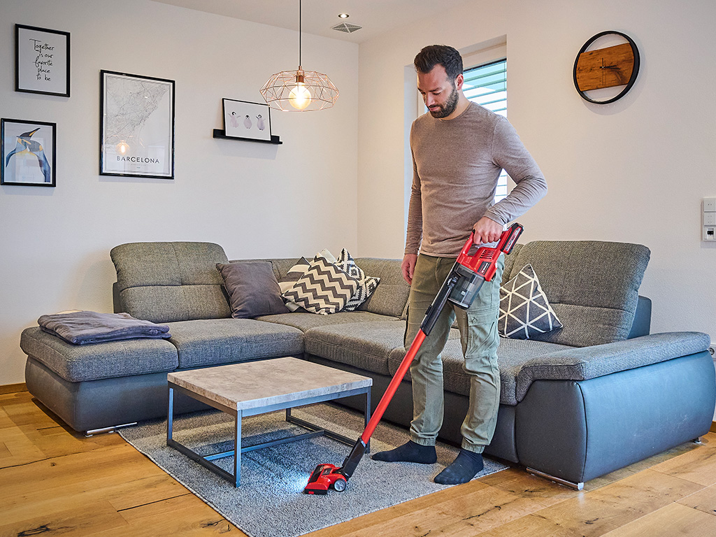 a man is vacuuming a carpet in a living room with the Einhell cordless stick vacuum cleaner