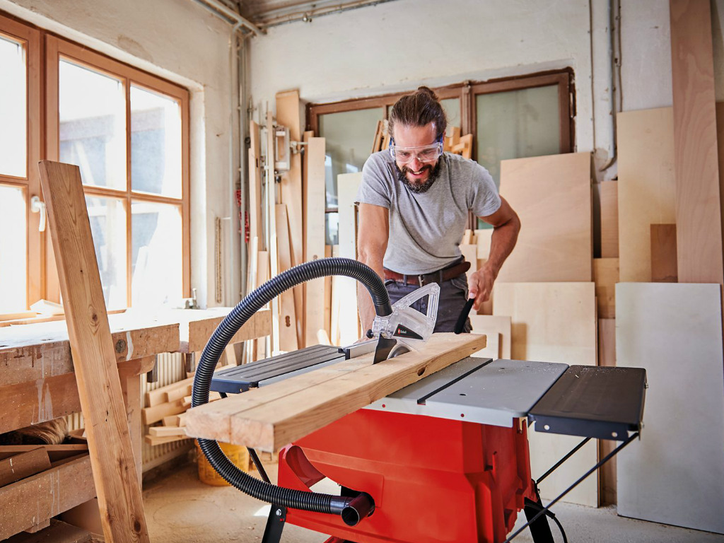 man cuts a wooden board in two with a table saw