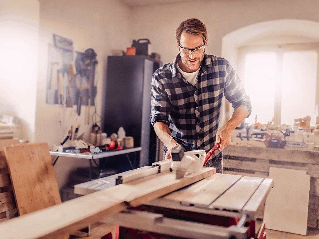 Ein Mann sägt Holz mit einer Tischkreissäge mit Parallelanschlag.