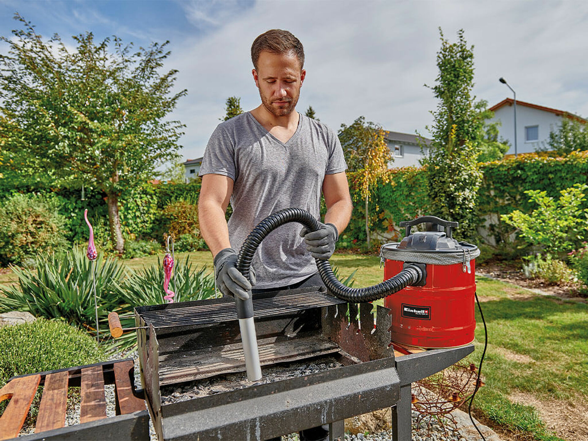 A man vacuums cold ash from a barbecue grill in the garden using the Einhell ash vacuum cleaner.