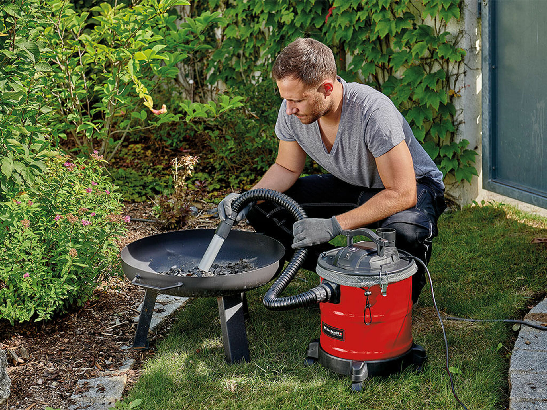 A man vacuums cold ash remains from a fire bowl in the garden using the Einhell ash vacuum cleaner.