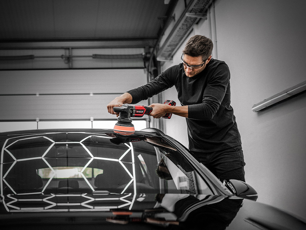 A man is polishing a car roof with an Einhell cordless polisher in a workshop.