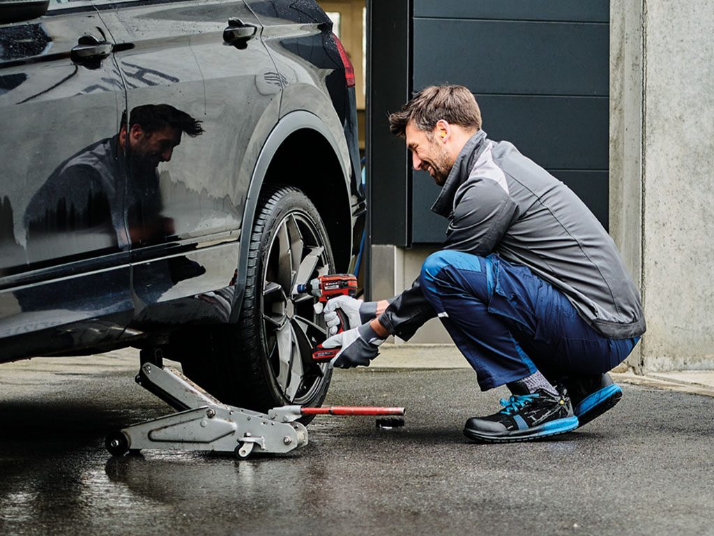 A man is tightening the screws of a car tyre with a Einhell cordless impact wrench