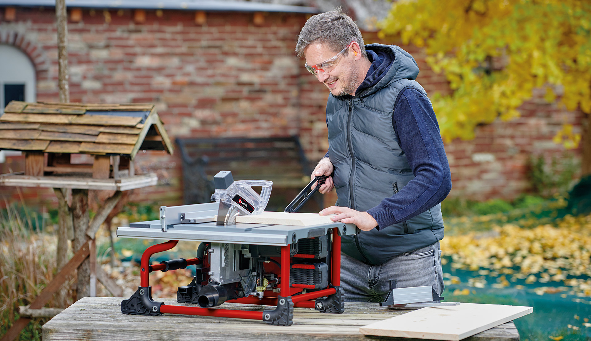Ein Mann arbeitet im Freien mit einer Tischkreissäge und führt ein Holzbrett über den Sägetisch.