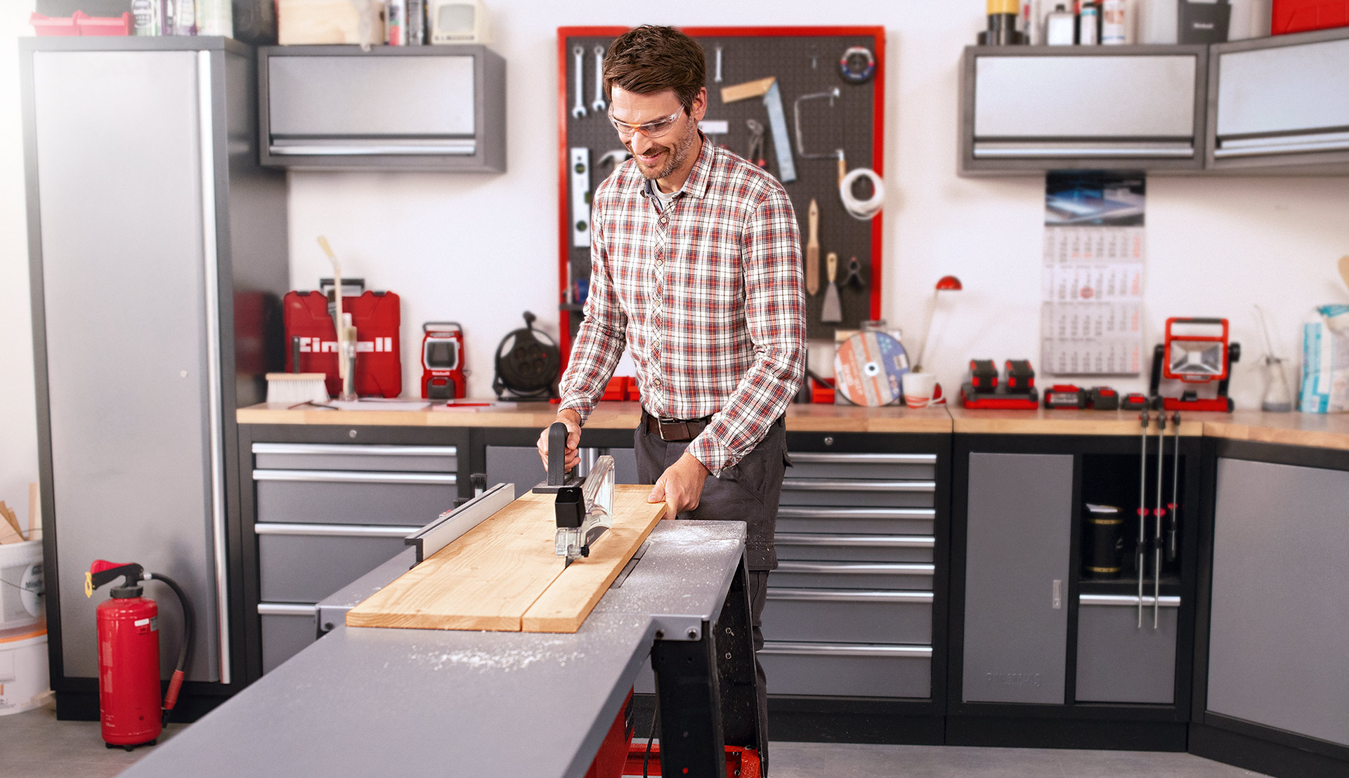 Ein Mann schiebt ein Holzbrett über eine Tischkreissäge in einer Werkstatt.