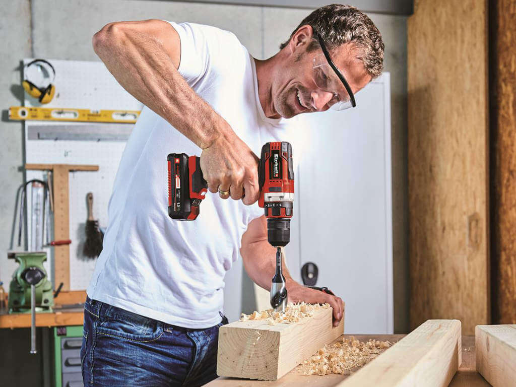 a man drills a hole in a wooden beam