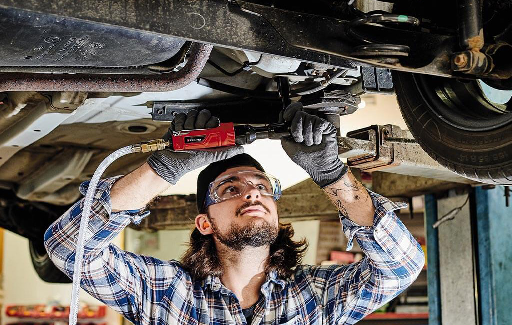 A mechanic uses an pneumatic impact wrench to work on the undercarriage of a vehicle.