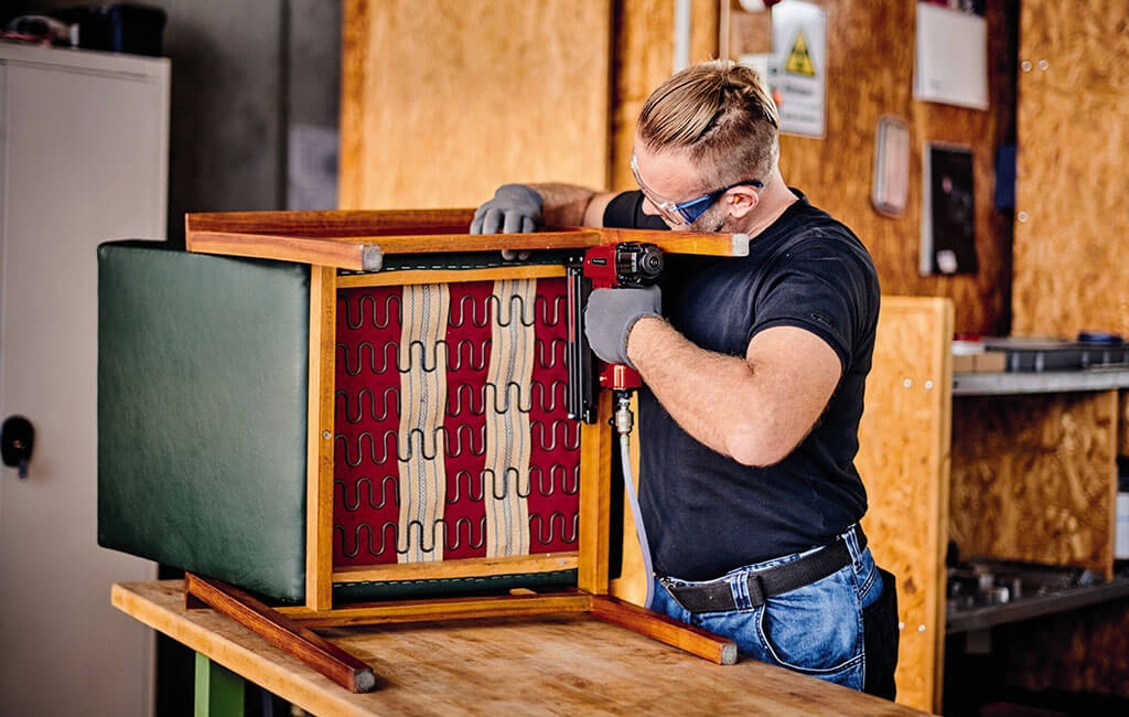 A man uses a pneumatic nailer to repair a chair.