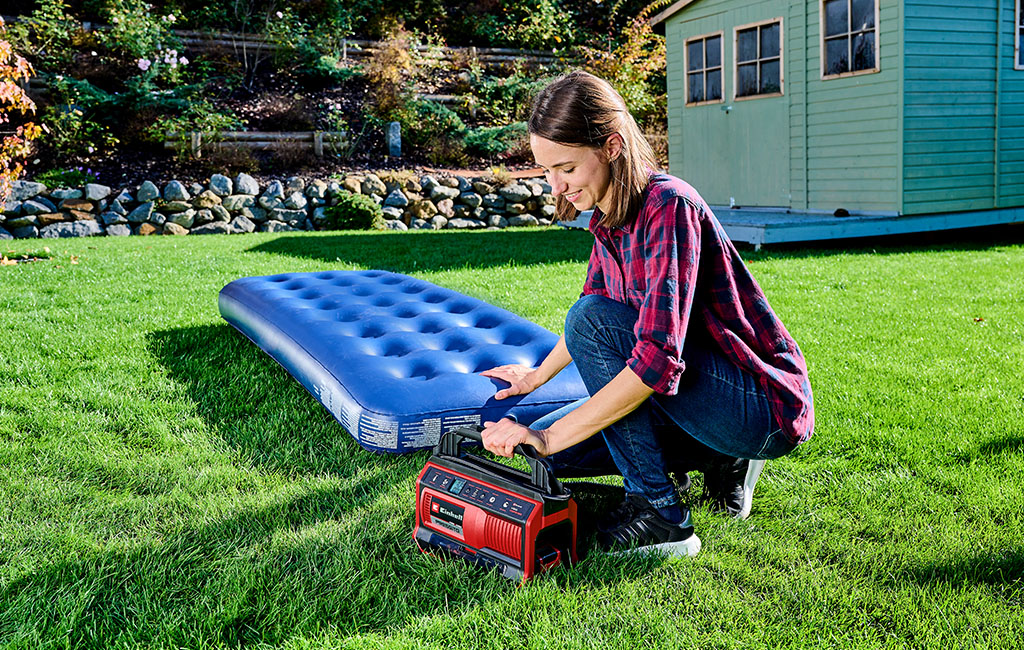A woman inflates an air mattress in the garden using the Einhell cordless compressor PRESSITO.