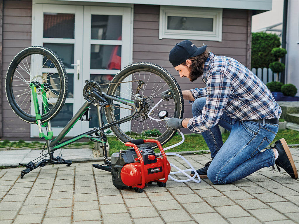Mann pumpt den Reifen seines Fahrrads mit einem Einhell Akku Kompressor auf und überprüft den Reifendruck.