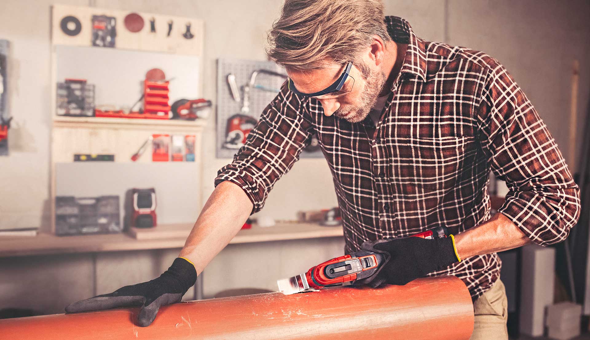 A man is cutting into a plastic pipe with a multifunction tool.