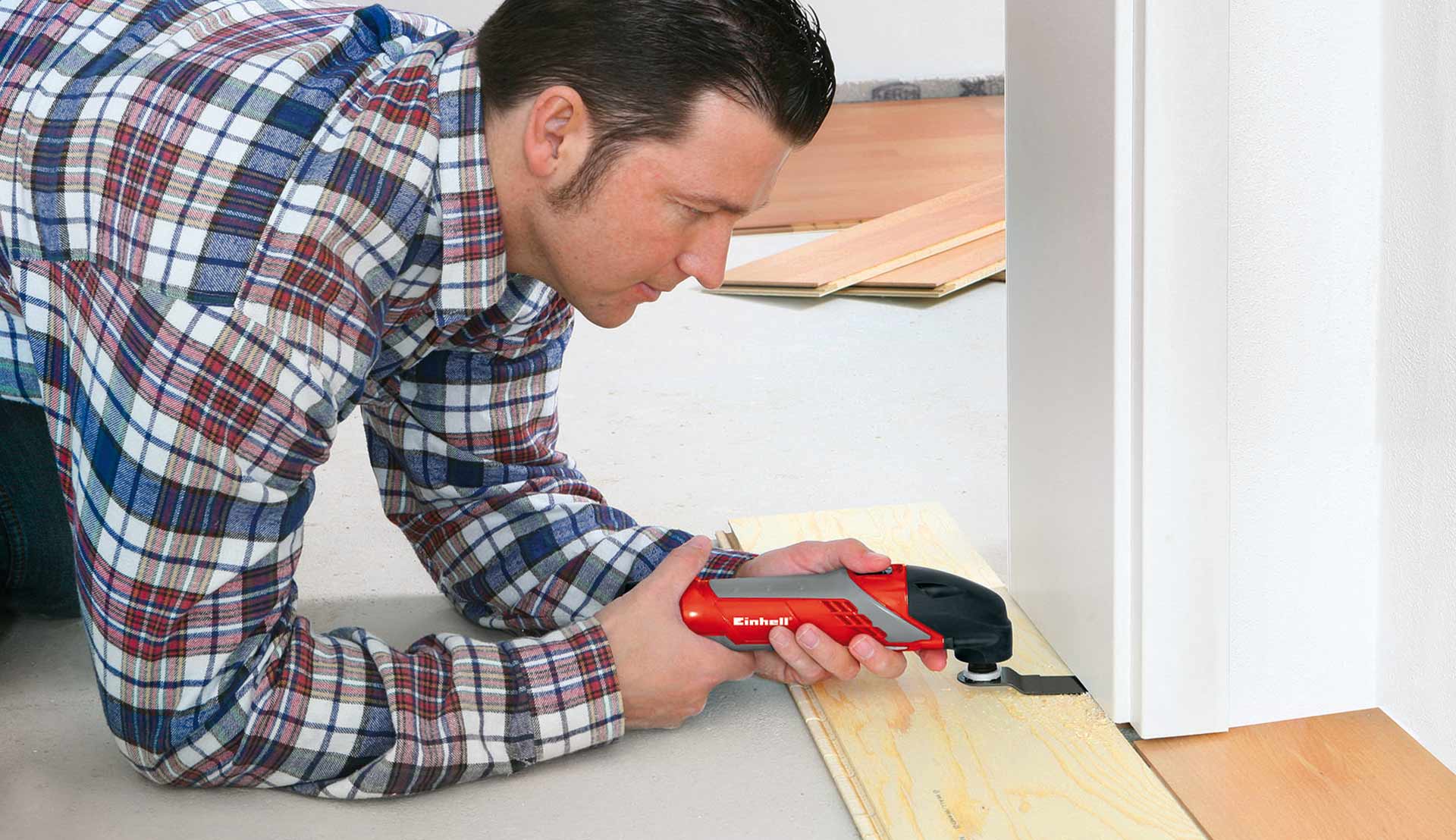 A man is sawing underneath a doorframe with a multitool equipped with a saw blade attachment.